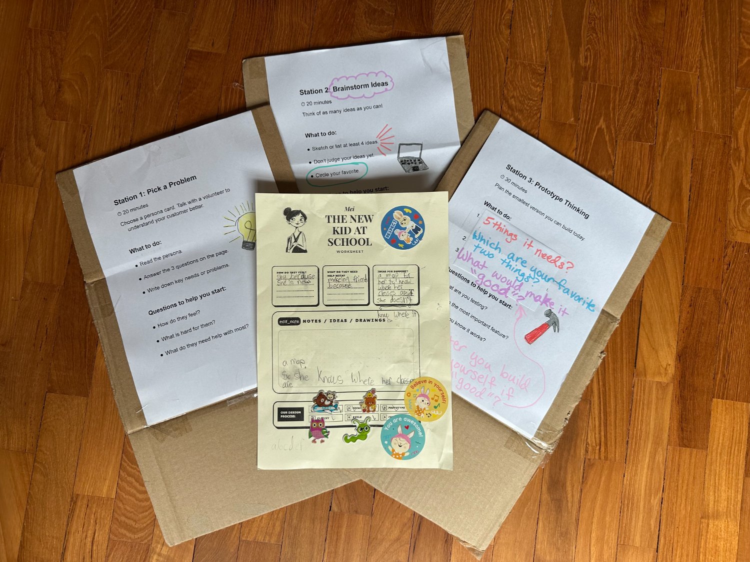 A spread of Builder's First station worksheets and a kid-completed persona sheet laid on cardboard boxes
